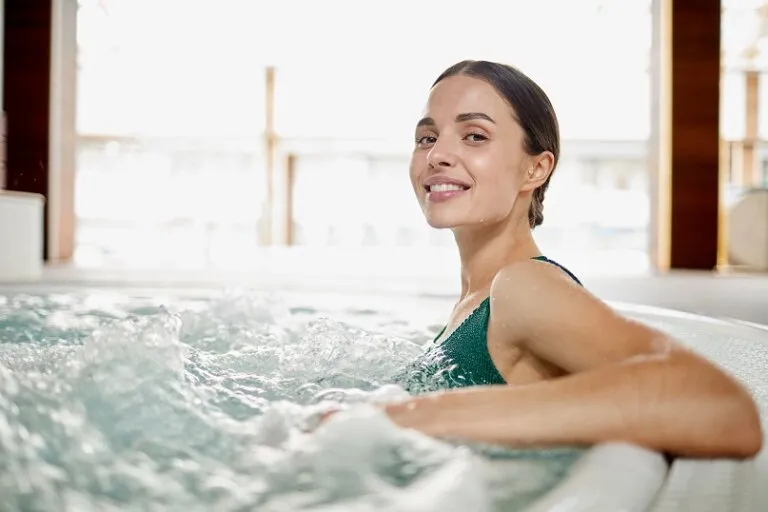 Woman relaxing in an indoor whirlpool tub, smiling while leaning against the edge with water jets surrounding her
